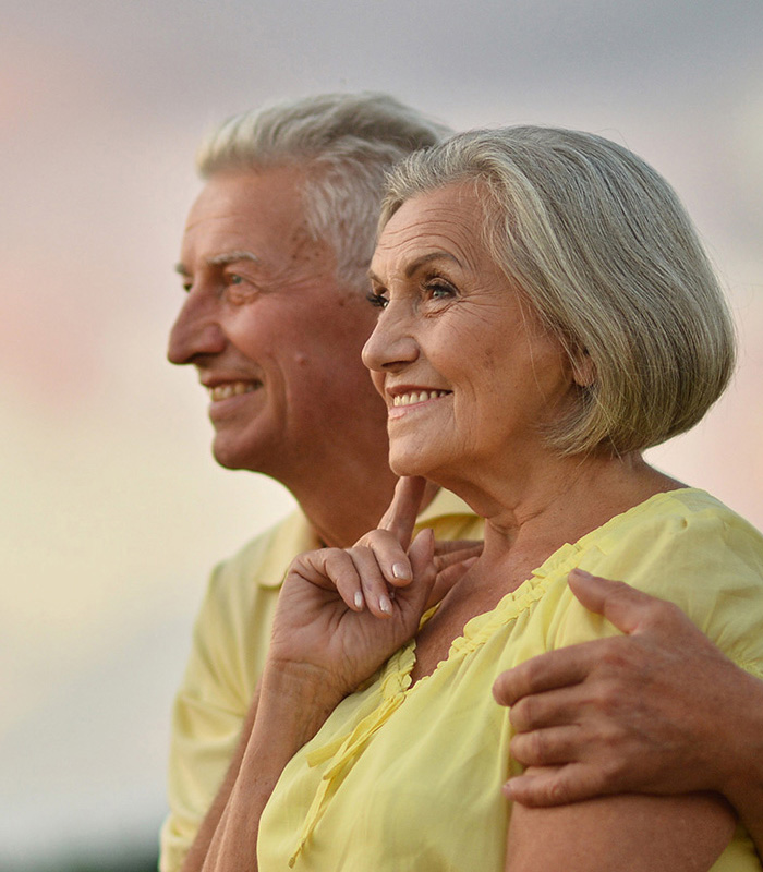A senior husband and wife smiling together looking out at a sunset.